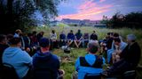 A group of dads seated around a campfire at sunset