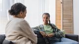 Smiling teenage girl talking with her mother while sat at on the sofa at home 