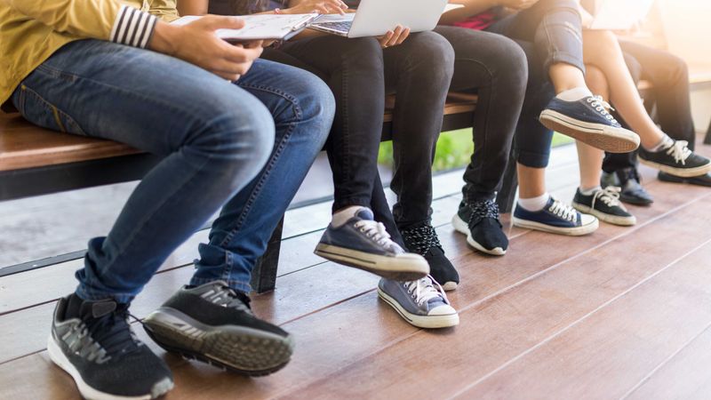 A group of young people sitting on a wooden bench using laptops and mobiles