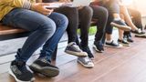 A group of young people sitting on a wooden bench using laptops and mobiles