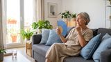 Elderly woman fanning herself whilst sat on the sofa