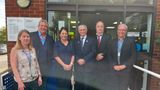 Six people stand outside the entrance to Sittingbourne Library and Family Hub for a group photograph. The group is positioned in front of the building's glass doors, with library and family hub signage visible on the brick exterior.