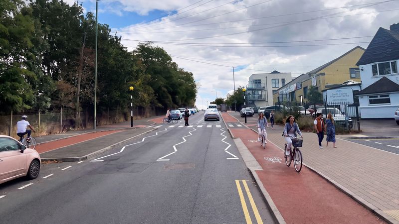 Artist's visualisation of proposed improvements at the A226 London Road and Oak Road junction in Stone, Dartford. The road includes new segregated cycle lanes on both sides, wider footways, upgraded pedestrian crossing points and revised road markings. Cyclists, pedestrians and vehicles are shown using the redesigned street layout.