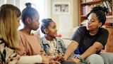 A mum and two daughters sit on a sofa and get support from another adult female