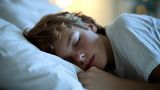 A close up image of a teenage boy sleeping at night