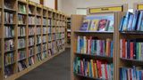 A close up of a bookshelf stacked with colourful books below a yellow sign saying "Novels". Further bookshelves in the background line the walls.