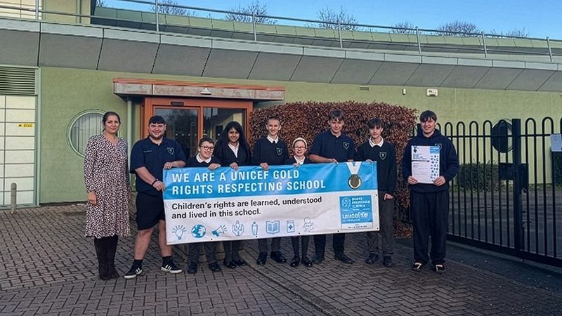 The headteacher and pupils from Grange Park School standing outside the school building holding a UNICEF award banner.
