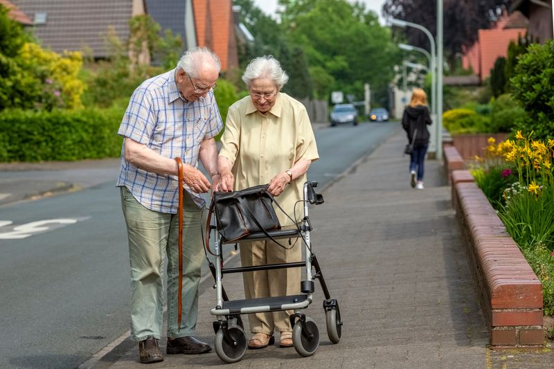 Two older adults on a residential street, checking a bag on a walking frame