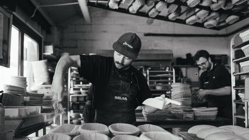 Head baker Josh Weston is seen making preparations in an industrial bakery for the loaves to be baked. He is sprinkling flour into tins