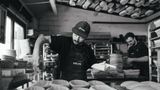 Head baker Josh Weston is seen making preparations in an industrial bakery for the loaves to be baked. He is sprinkling flour into tins