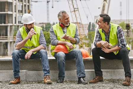 Three construction workers sitting down on site eating sandwiches