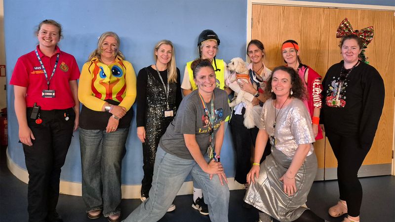 A group of teachers wearing fancy dress. One is holing Hythe Bay School's therapy dog Watson who is dress as an astronaut