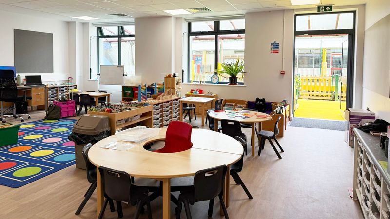 A brand new primary school classroom with round tables, plastic black chairs and a colourful play mt