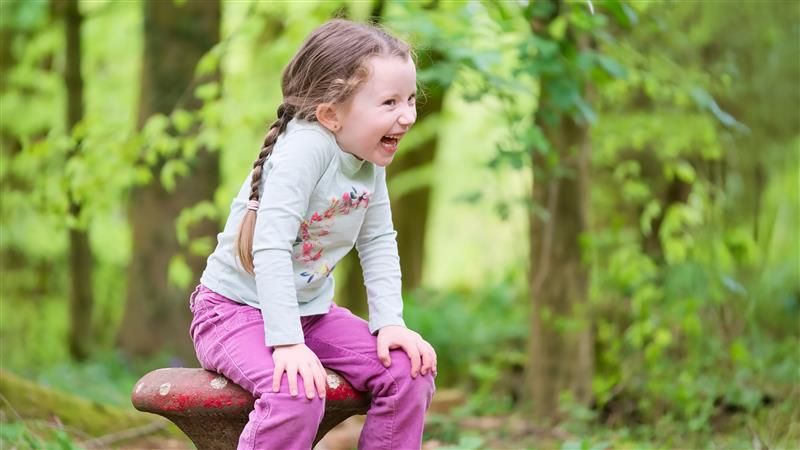 A young girl sitting and laughing with her hands on her knees in a woodland forest 