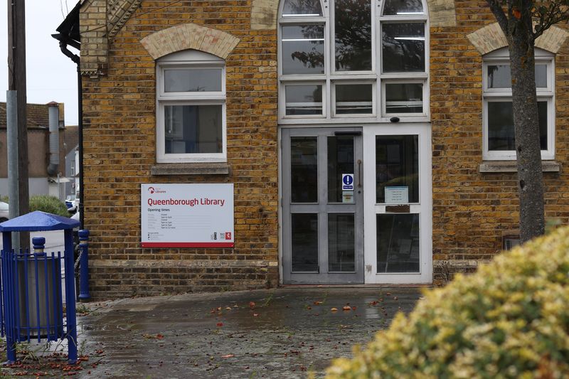The entrance to Queenborough Library. A white sign with 'Queenborough Library" is to the left of the door with the building opening times