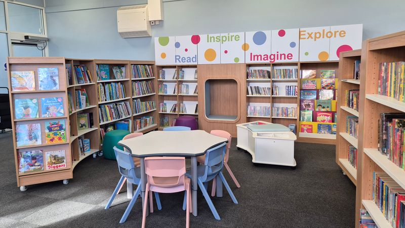 The colourful new children's section at Temple Hill Library has a book nook to sit in, a table and chairs in the middle and is surrounded by bookshelves. The words read, inspire, imagine and explore are written on the shelves 