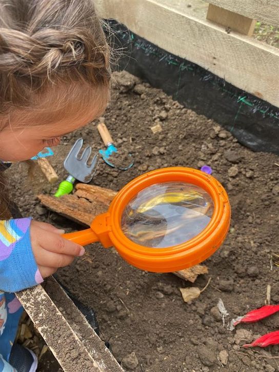 Child with blond braids looks at soil through an orange magnifying glass