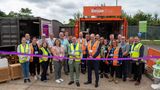 A group of people in yellow and orange hi-vis smile towards a camera. Someone at the front centre is cutting a ribbon.
