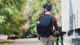The back of a man wearing a helment and a backpack and standing next to a bike.