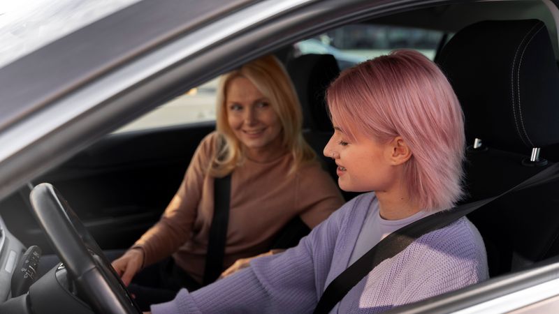 Young woman with pink hair sitting in a car with a driving instructor