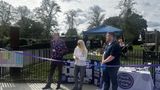 Three people stand in front of a purple ribbon in a park.