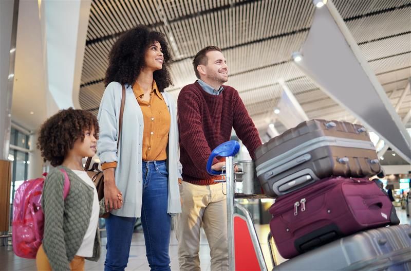 Family walking through airport with trolley stacked with suitcases