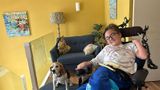 Lucie Lewis in her wheelchair at home next to her beagle Poppy who is sat on a blue sofa stool