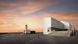 Exterior of Turner Contemporary in Margate at sunset, showing the modern glass‑fronted gallery building, wide steps and the historic clock tower on the seafront.