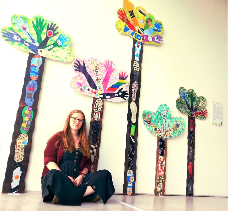 Artist Hannah Whittaker sits in front of the colourful tree designs that form Draw Hope