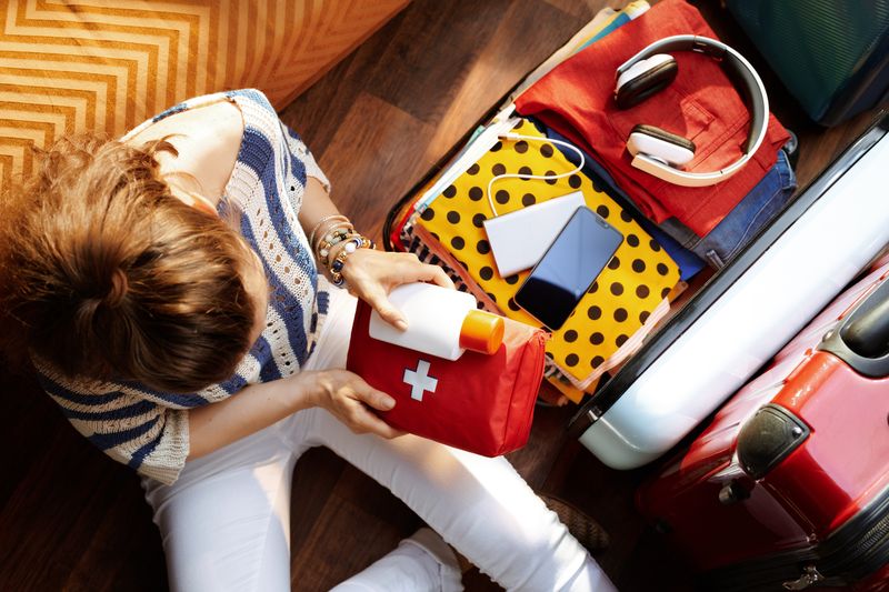 Woman packing first aid kit and sunscreen into open suitcase