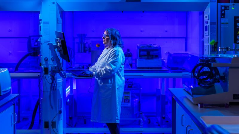A scientist works in a laboratory. It is lit entirely in a blue light 