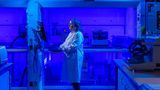A scientist works in a laboratory. It is lit entirely in a blue light 