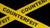 Cross of yellow ticker tape with word 'counterfeit' on it against black background