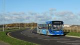 A photo of a blue bus driving on a road.