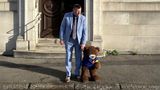 a photo of a man in a blue suit holding hands with a bear about to cross the road.