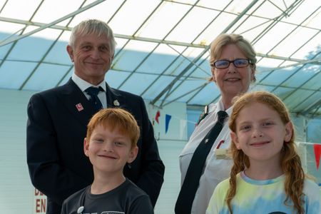 Two smiling children with two smartly dressed adults behind them at an indoor swimming pool 