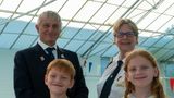 Two smiling children with two smartly dressed adults behind them at an indoor swimming pool 