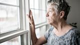 Lonely elderly woman looks out of window