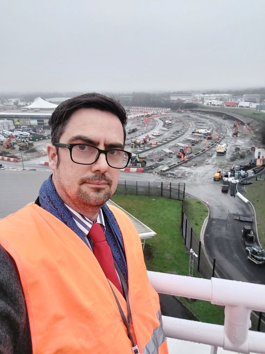 Neil Baker, KCC Cabinet Member for Highways and Transport, in an orange hi-vis jacket, looks over the site at Eurotunnel