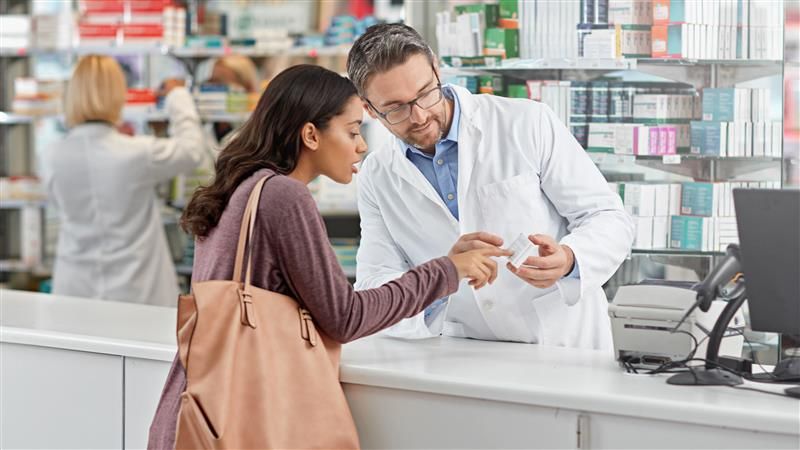 Male pharmacist points out advice on medicine packaging to a woman customer