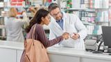 Male pharmacist points out advice on medicine packaging to a woman customer