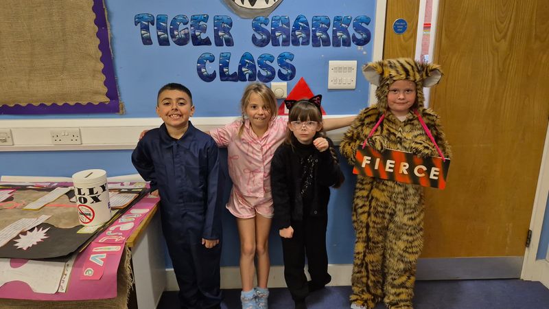 Four children standing under a sign saying Tiger Sharks Class. Each child is dresses as a word. The child on the right is holding at sign representing her word saying 'Fierce' 