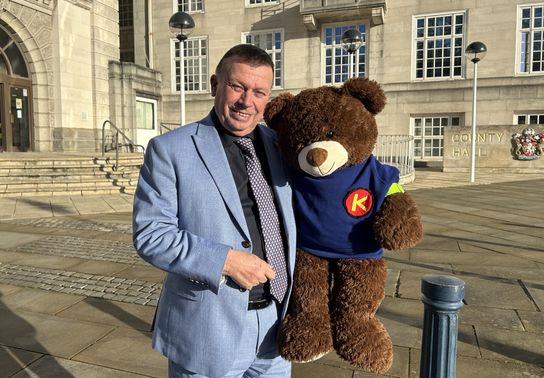 A photo of Peter in a blue suit smiling at the camera and holding Kip the Bear.