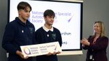 Two teenage boys in Grange Park uniform holding a plaque . Beverley Fordham is stood on the right clapping after presenting them with the award