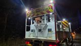 "A highway maintenance vehicle positioned on a road during overnight maintenance works, with reflective safety markings and illuminated warning signs visible."