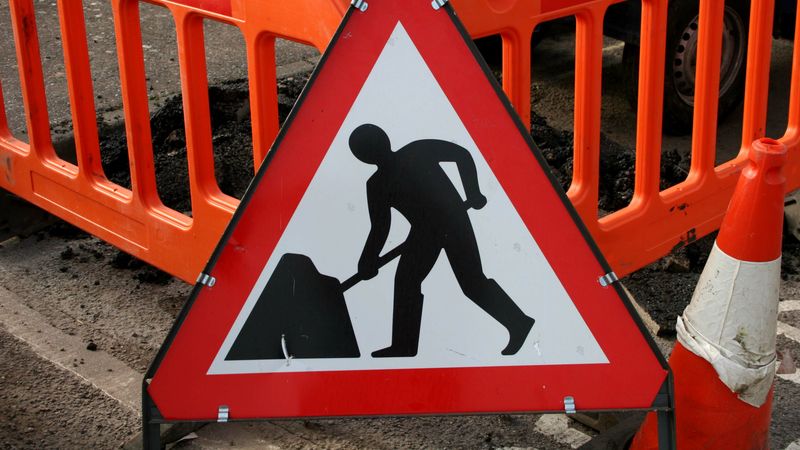 A roadworks warning road sign in front on two highway barriers