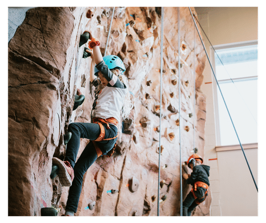 Two children in safety harnesses using a climbing wall