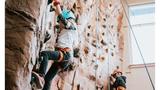 Two children in safety harnesses using a climbing wall