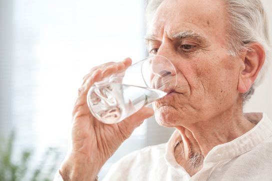 Elderly man drinks a glass of water