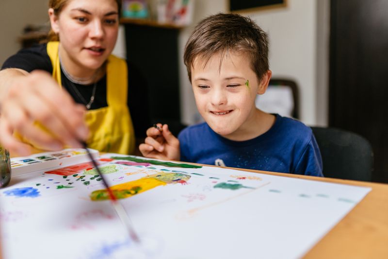 Teacher works on a painting at a desk with a young student